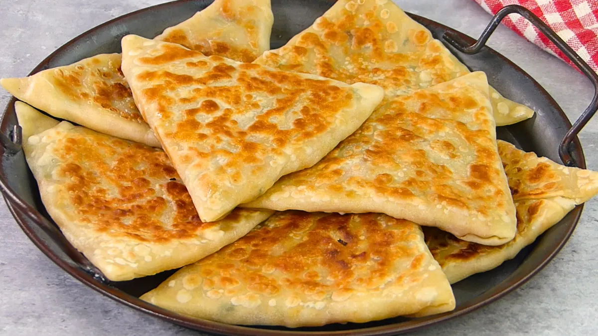 Afghan bolani slices on a wooden board, served with yogurt dip